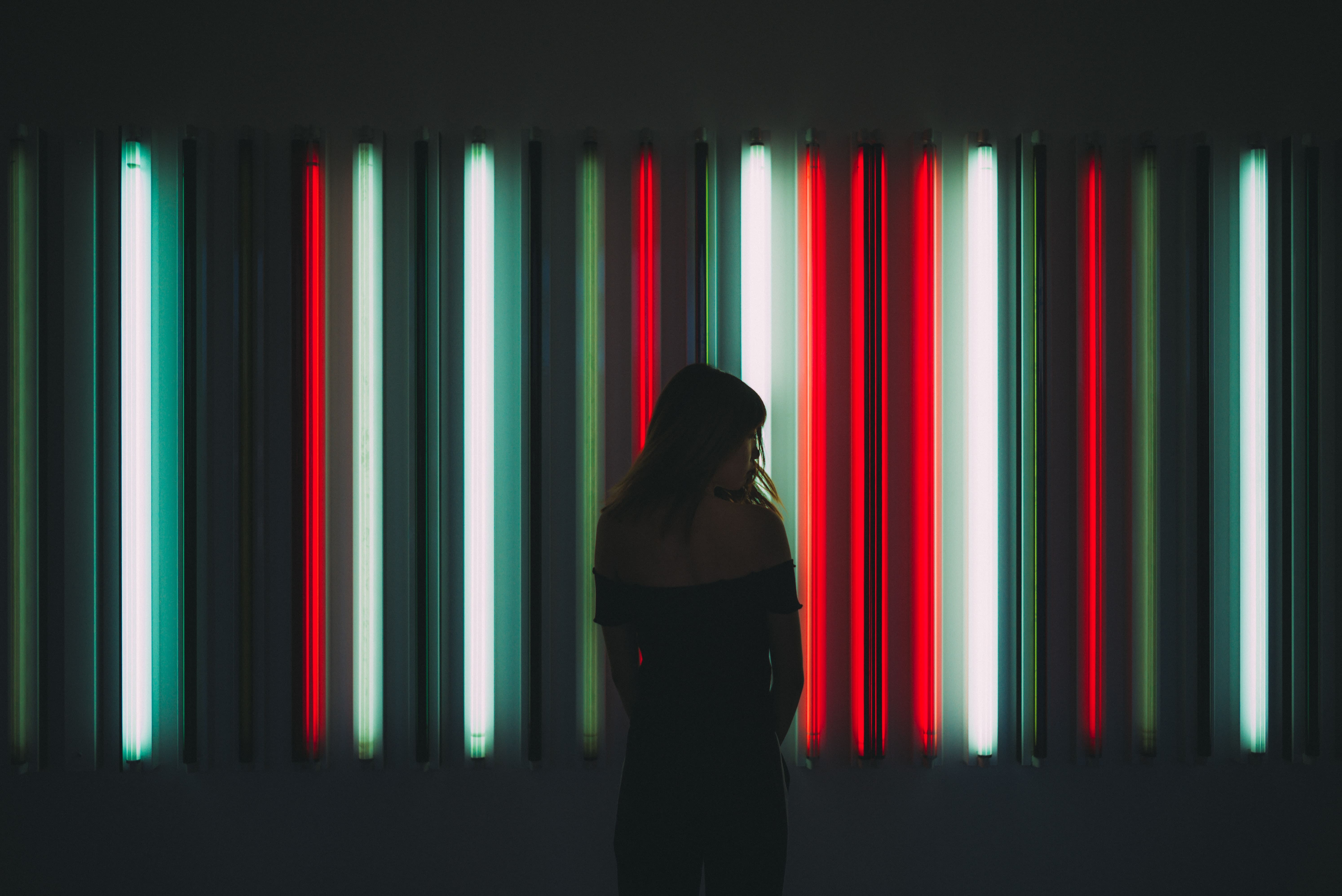 A woman's silhouette in front of a wall of white and red fluorescent light bulbs.