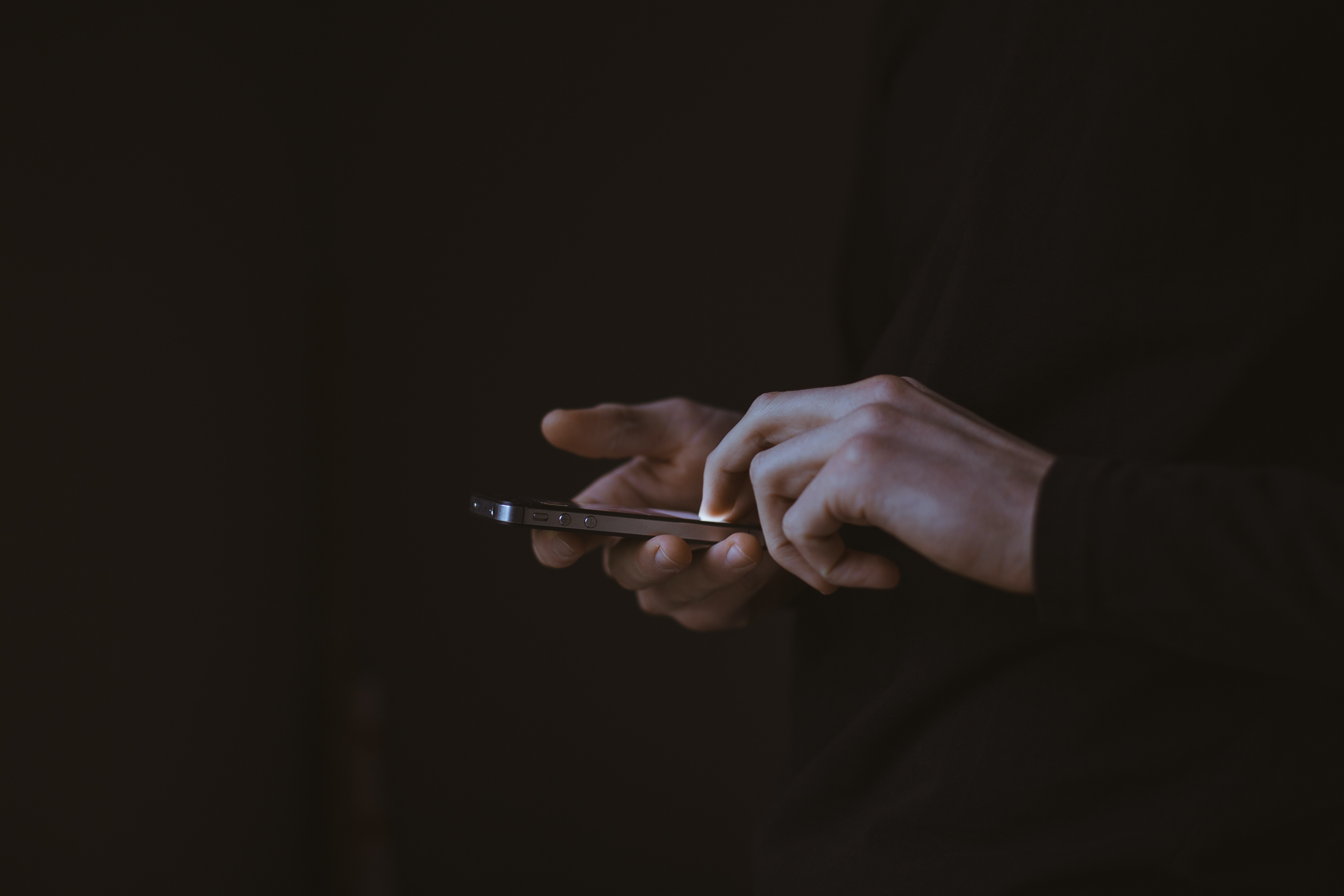 A man holding a smartphone in his hands overlayed on a dark background.