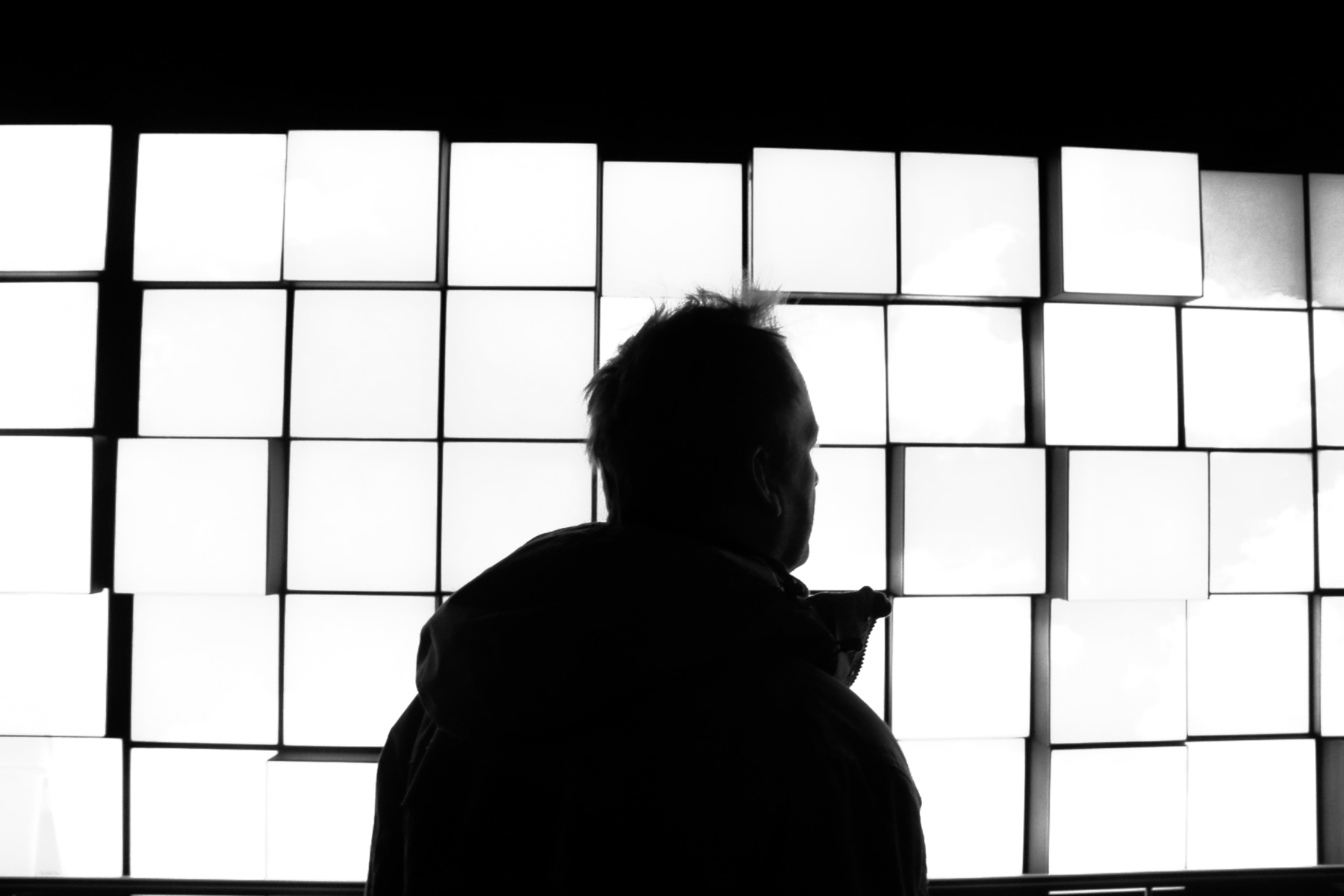 A silhouete man walking behind a row of tall windows.